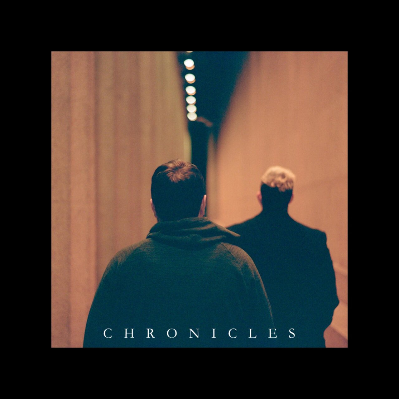 Two men walking in a dimly lit corridor, back view, with the word 'CHRONICLES' at the bottom.