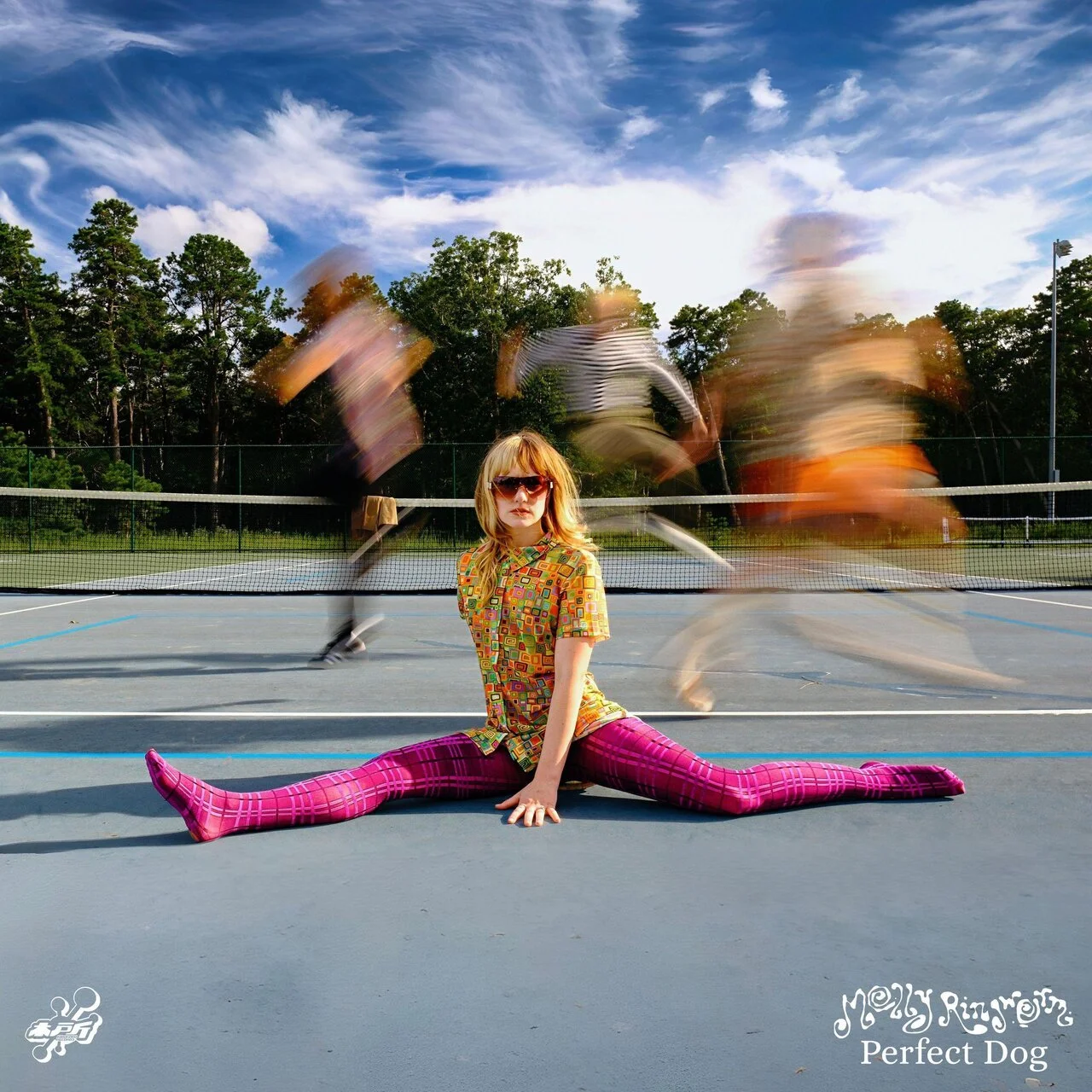 A woman sitting on the tennis court with her legs spread out in a split, wearing a colorful patterned dress and pink checkered tights, with her hair down and wearing sunglasses. Blurred figures are moving behind her on the court, and there is a blue 