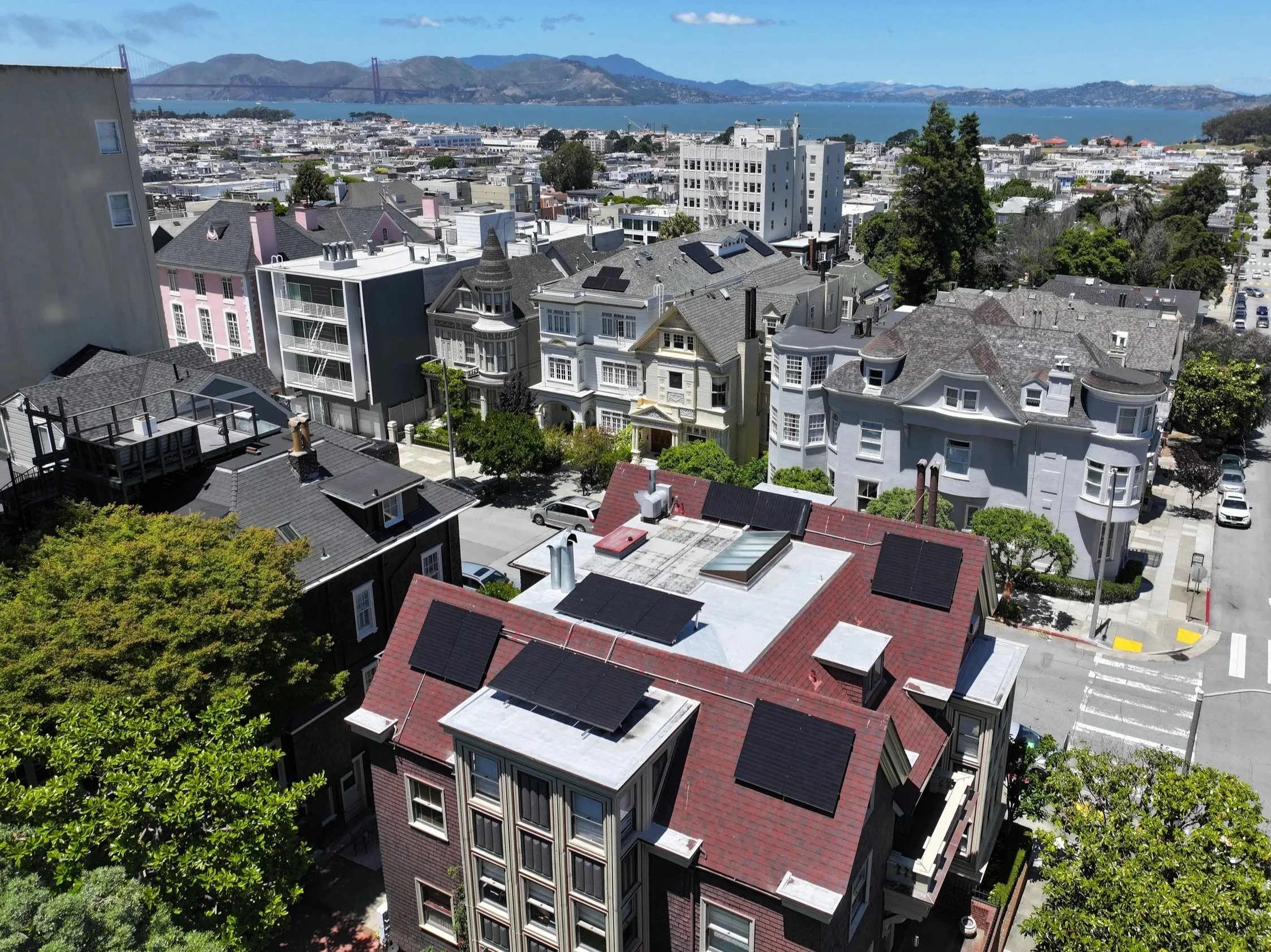 A view of a cityscape with densely packed houses and buildings, a water body in the background, and hills and a bridge in the distance.