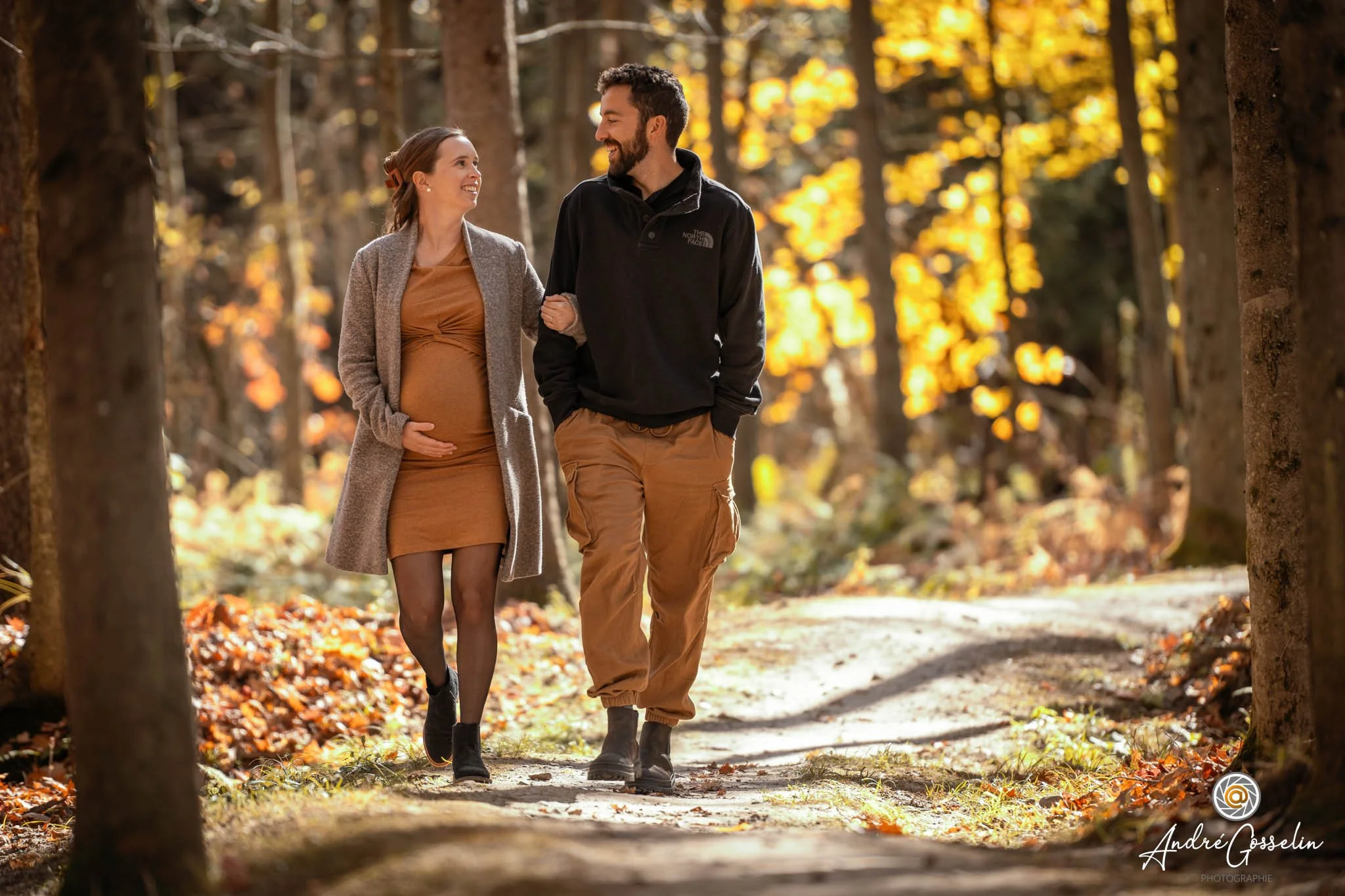 Un couple marche dans une forêt aux couleurs automnales, il est heureux et regarde l'un l'autre, la femme est enceinte, ils semblent se promener en profitant de la nature.