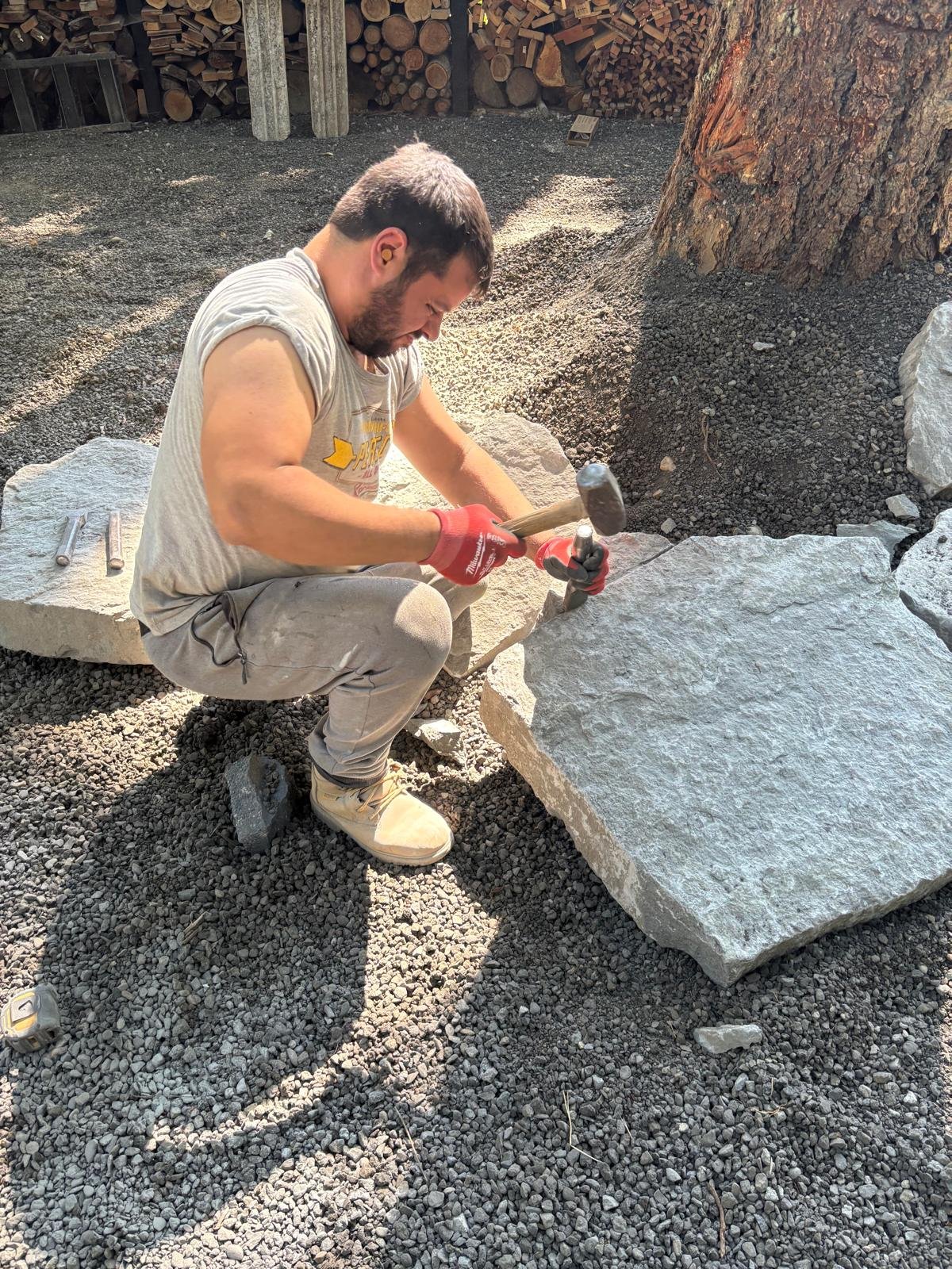 Professional stone masons hand-chisel natural stone during a custom construction project, highlighting expert masonry craftsmanship, durable materials, and high-end stonework for home remodeling and construction services.