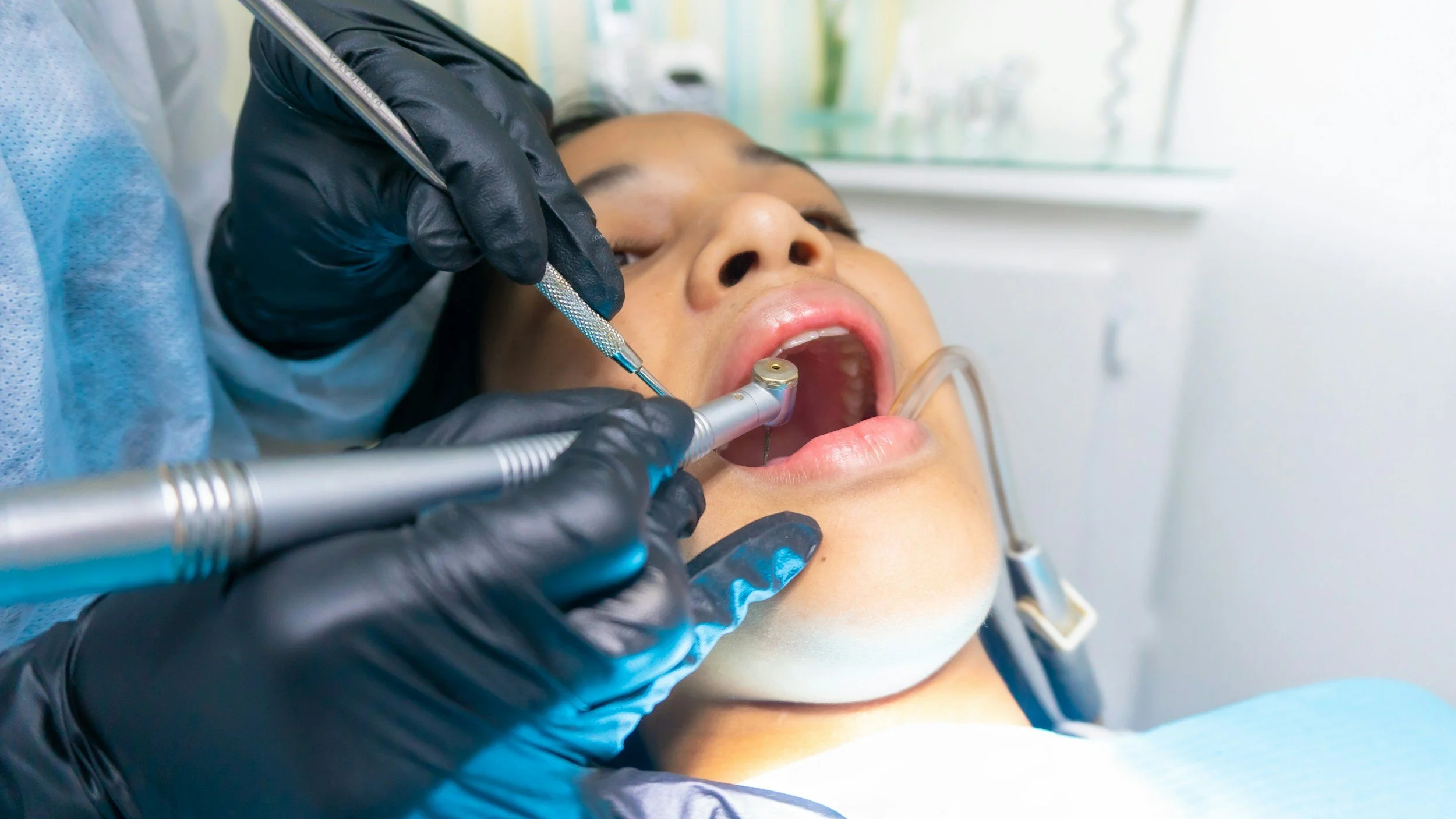 Dentist performing a dental procedure on a patient lying in a dental chair, with dental tools and equipment visible.