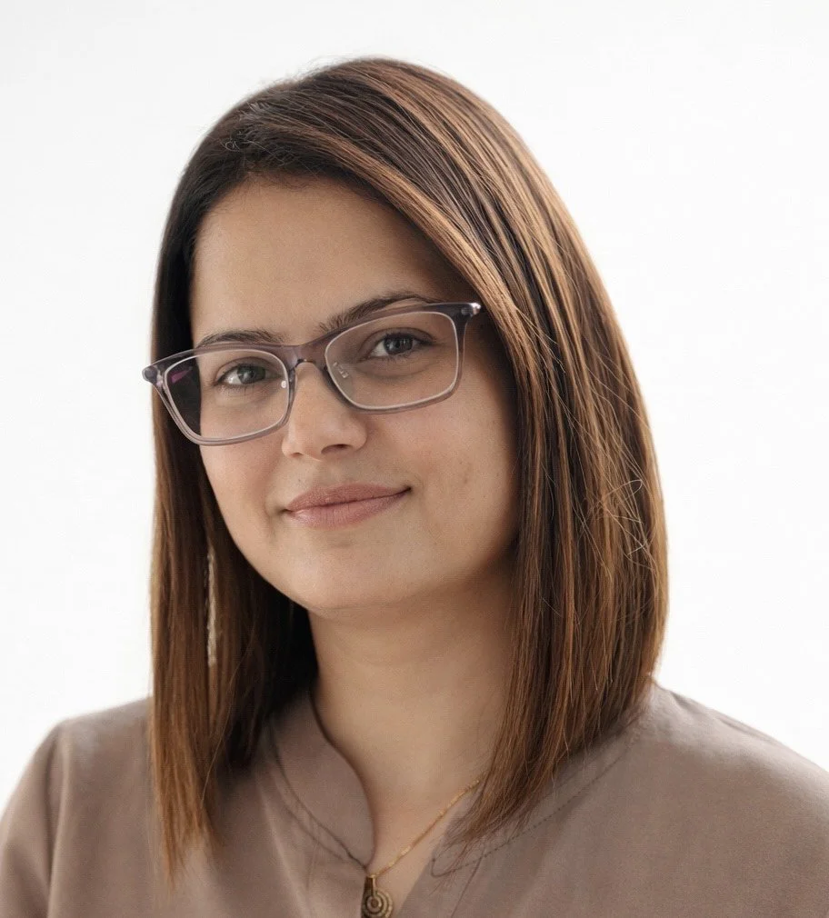 A woman with shoulder-length brown hair, wearing glasses and a beige top, smiling slightly against a plain white background.