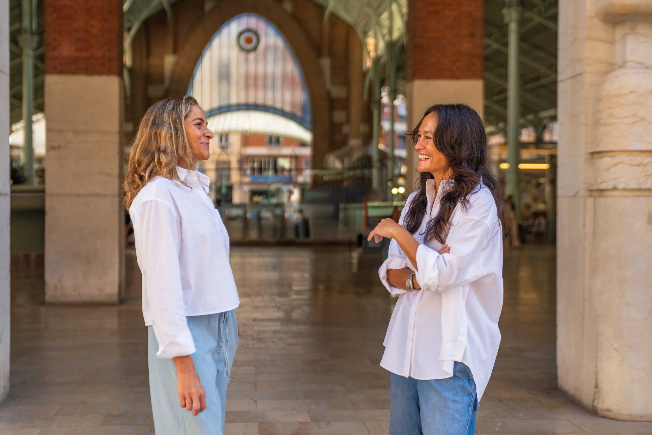 Maria Alacreu and Stephanie Kirtley, founders of Encantada World, talking and laughing in Valencia's Mercado de Colón