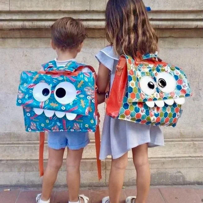 Two young children with matching monster backpacks, ready for their first day at a new school in Spain