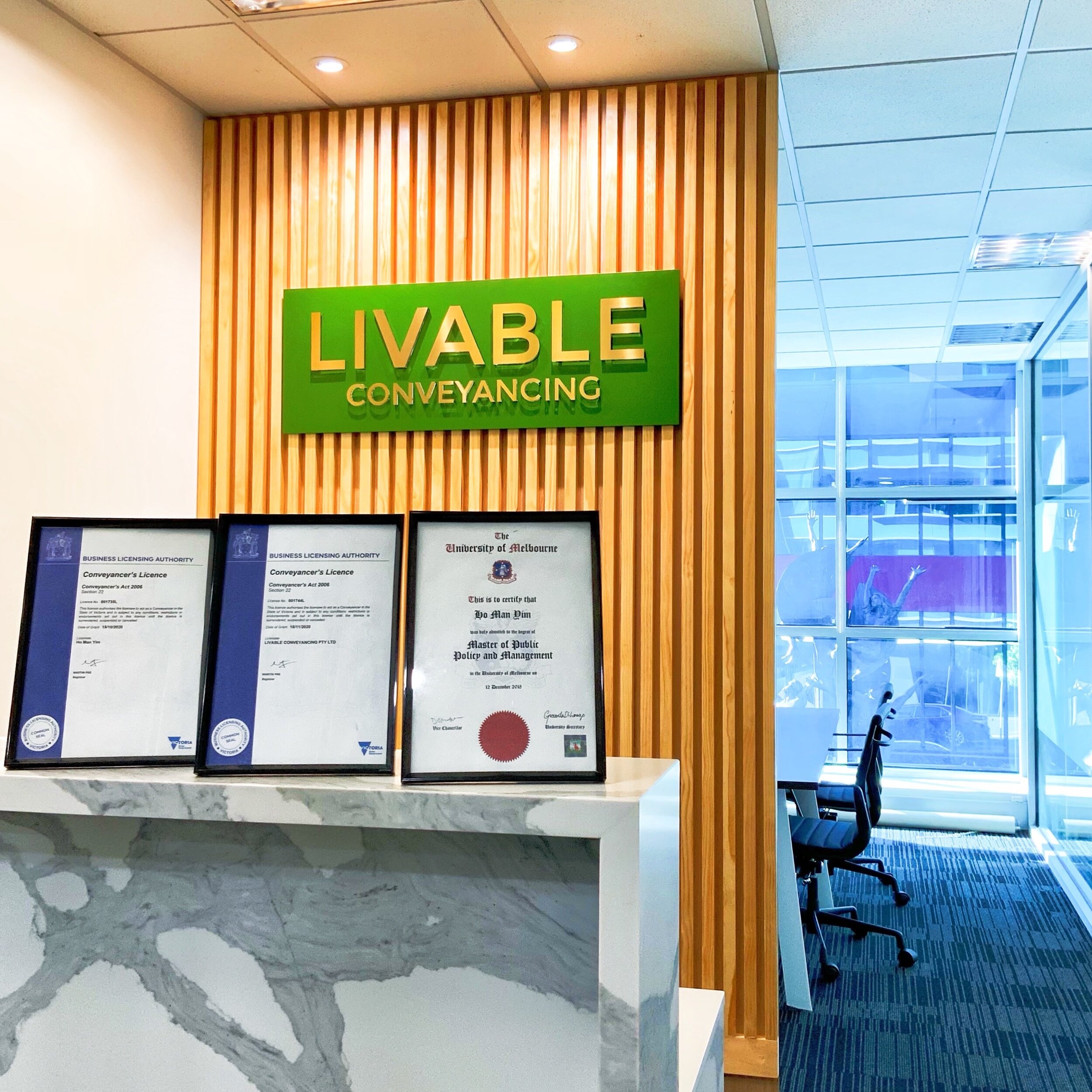 Office reception area with "Livable Conveyancing" sign, framed certificates, and a meeting room visible in the background.