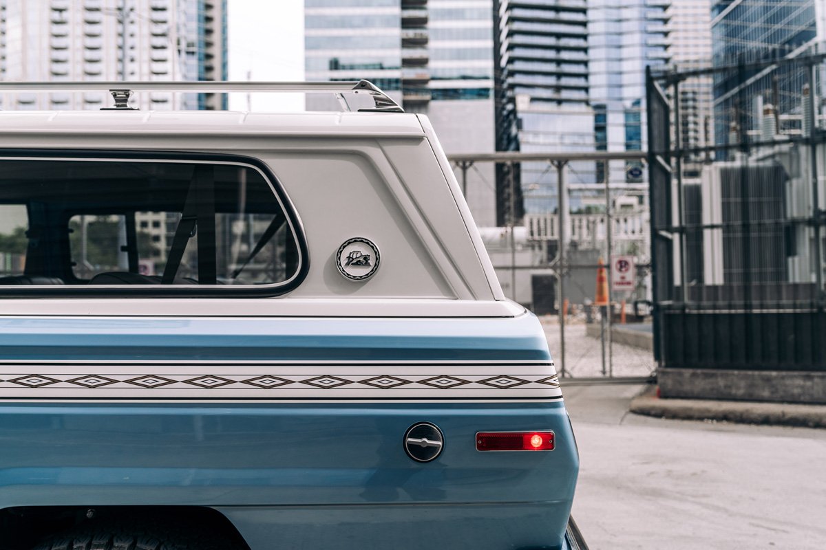 Rear side of a vintage blue and white camper trailer with a city skyline in the background.