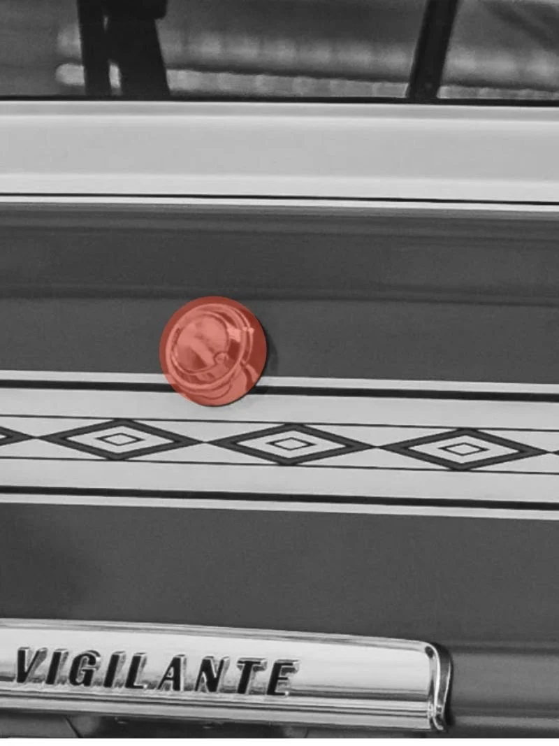Close-up of a vintage vehicle with decorative stripes, a red circular object, and a chrome emblem that reads "VIGILANTE".