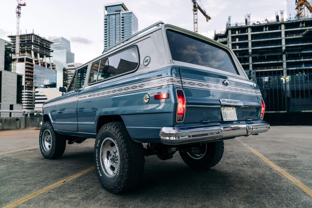 A vintage blue Jeep Cherokee parked in an urban setting with skyscrapers under construction in the background.