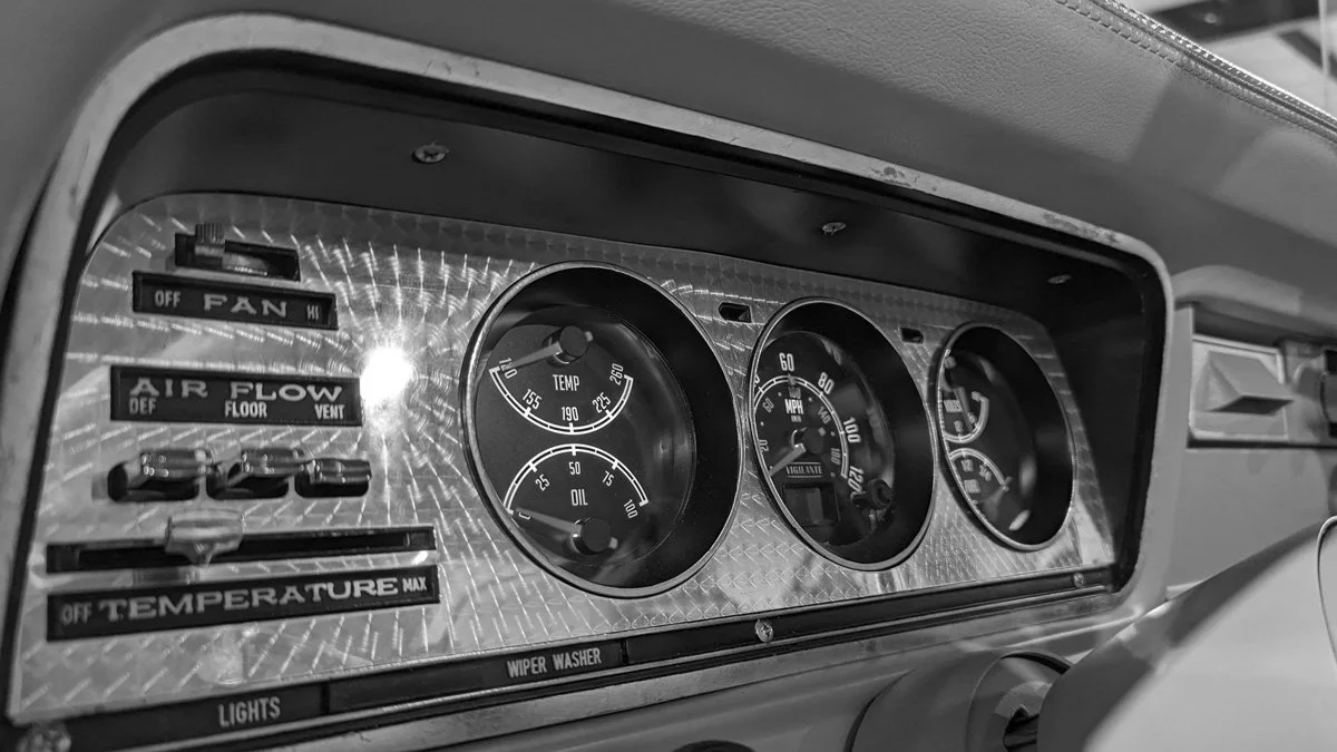 Close-up of vintage car dashboard with gauges, switches, and dials, including temperature, oil, and speedometers, with labels for fan, air flow, and lights.