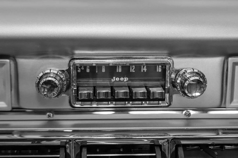 Black and white photo of a vintage Jeep car radio with knobs on each side and push buttons below the dial.