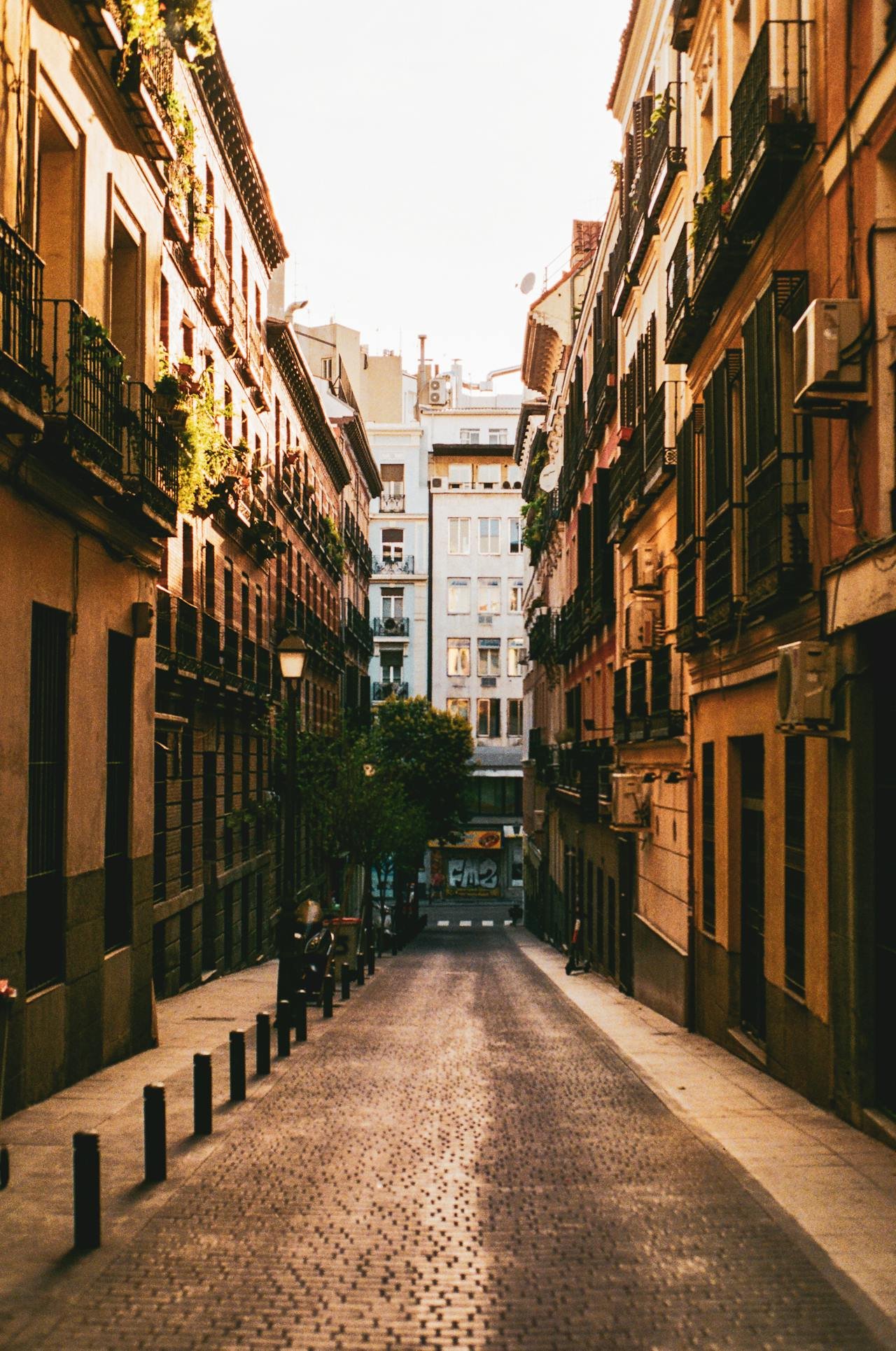 Callejón urbano empedrado con edificios antiguos y balcones al atardecer.