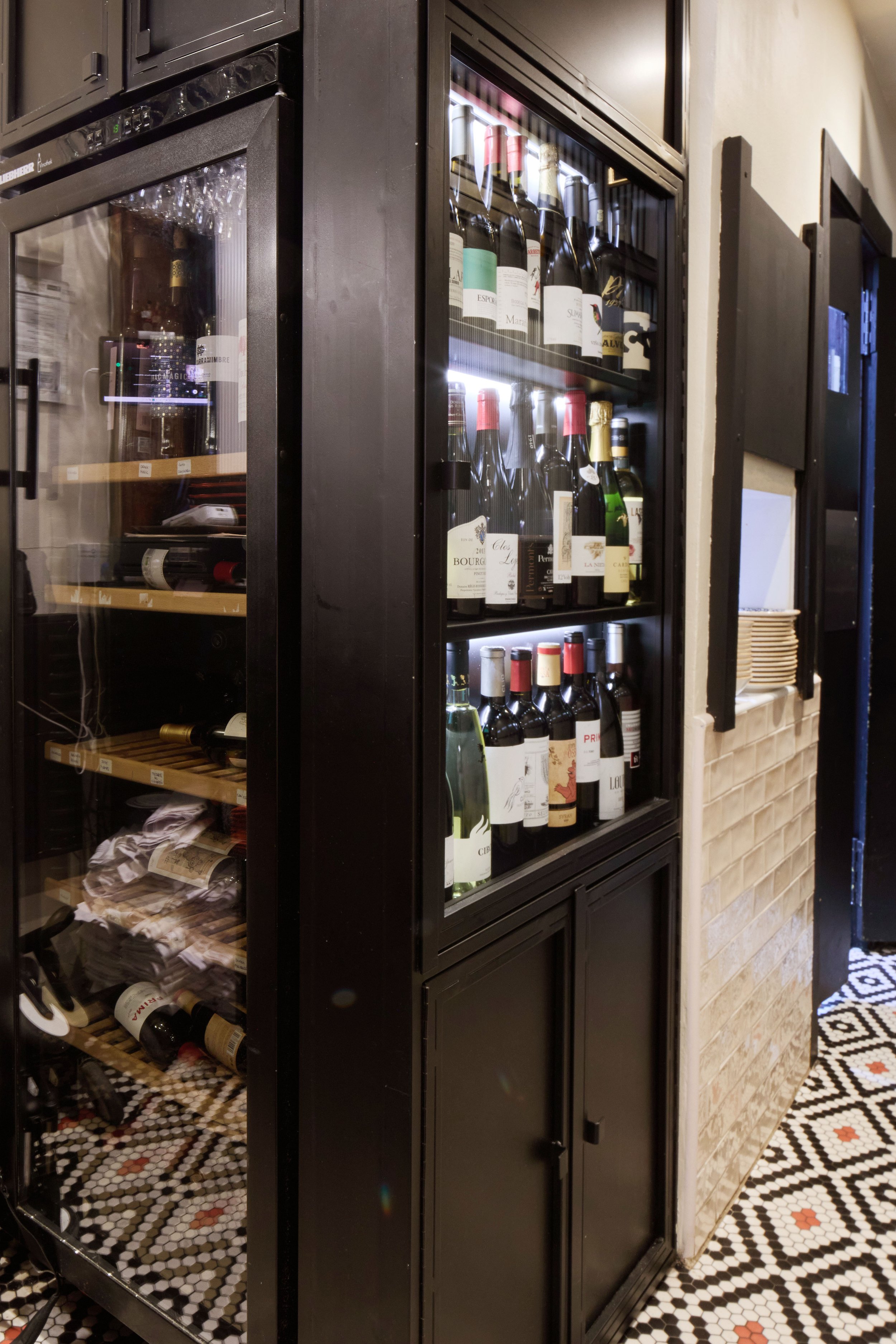 Enfriador de vinos con botellas en un restaurante moderno con piso de mosaico blanco y negro.