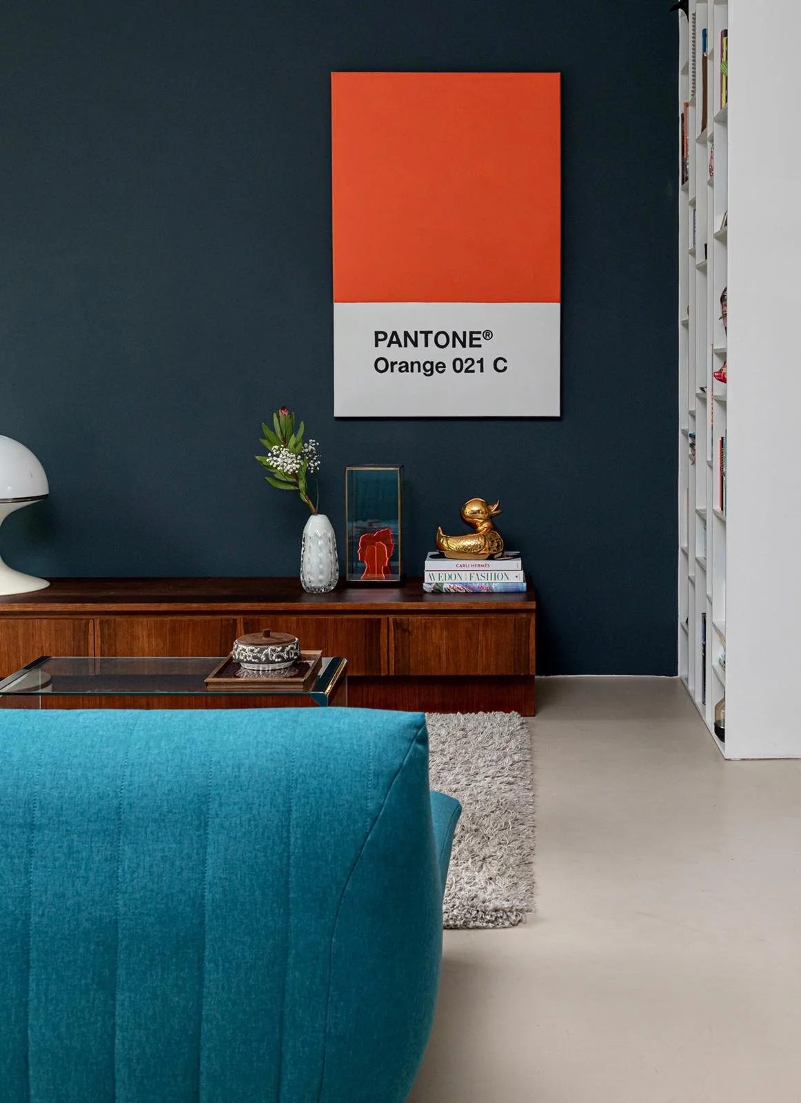 CharlotteMixt interieurontwerp Vught. Mixen van stijlen, blauwe bank, bruine vintage sidetable, oranje schilderij pantone 021 aan de muur, vakkenkast, kunst op sidetable, crème vloerkleed met glazen salontafel.