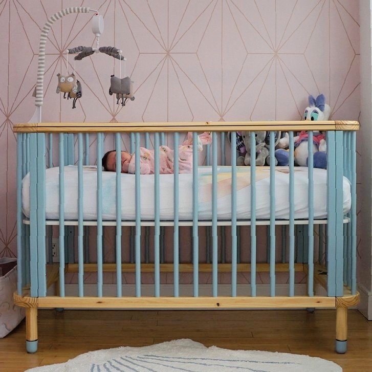 a shot of a baby crib in nursery room against pink and gold wallpaper