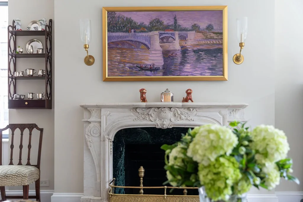 Carved marble fireplace with brass sconces and framed artwork in a Sutton Place apartment