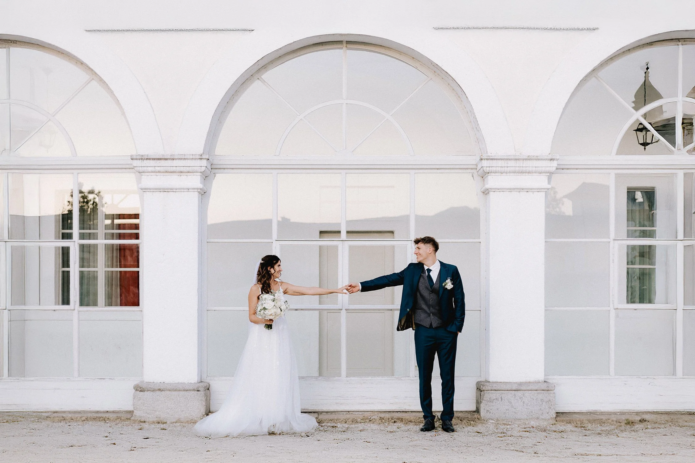 A bride and groom holding hands in front of a white arched building.