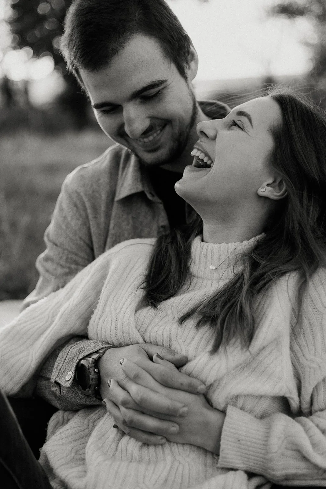 A black-and-white photo of a smiling woman and man gazing at each other outdoors, sharing a joyful moment.