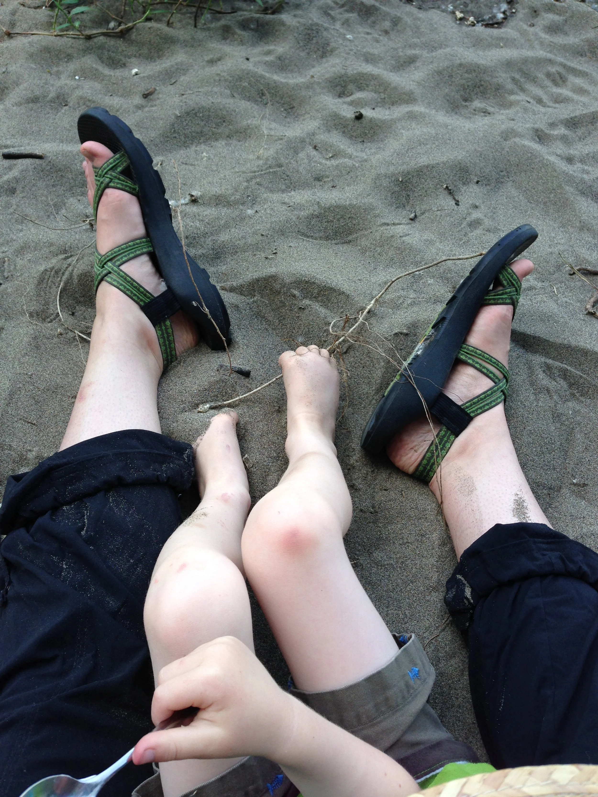 Mama and toddler in lap with sandaled feet in the sand