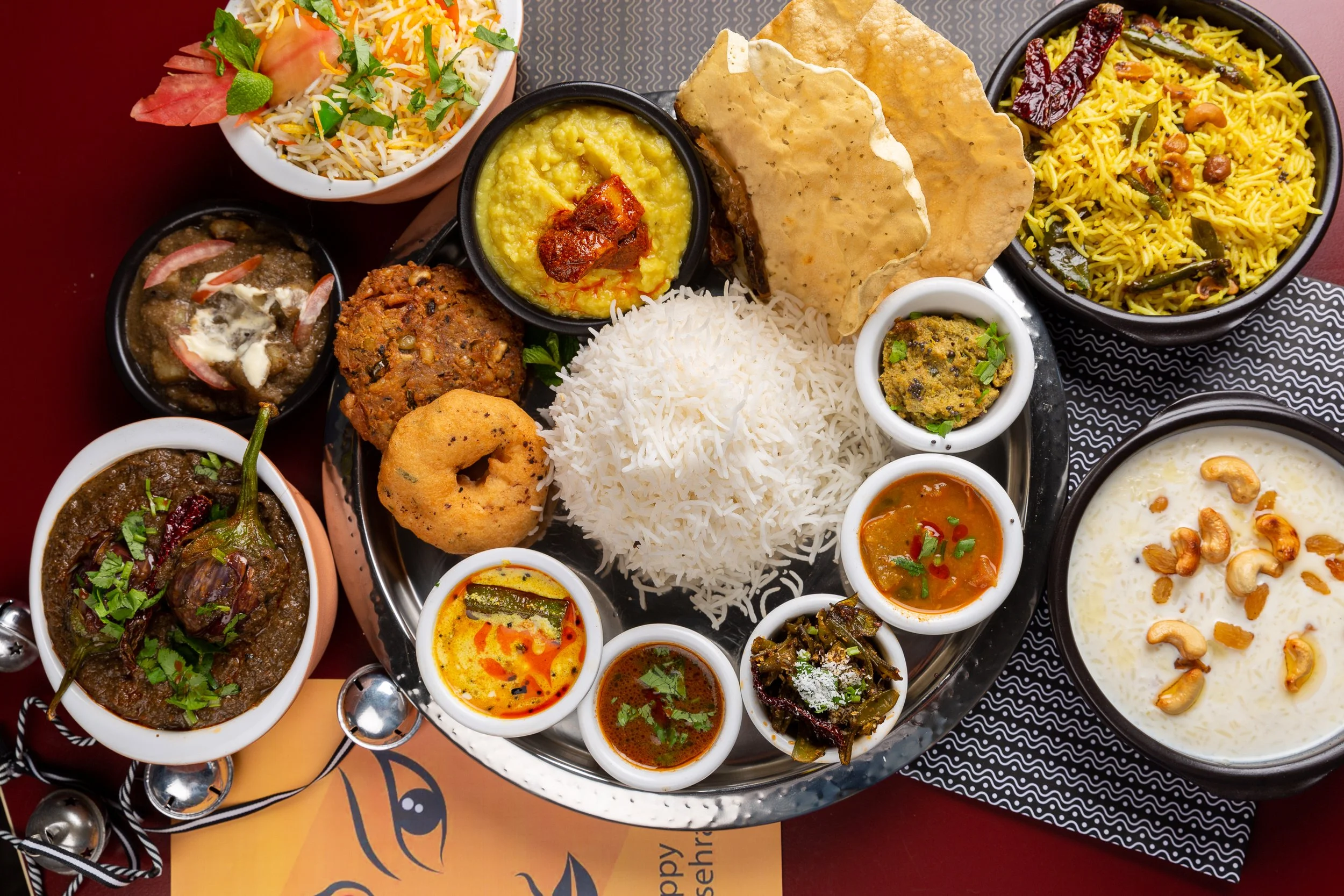A tray of traditional Indian dishes including rice, lentil curry, vegetable curries, and various small bowls of sauces and chutneys.