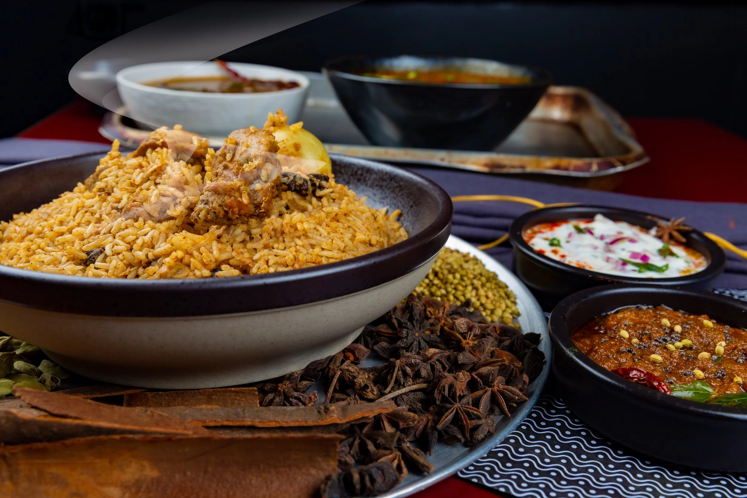 A variety of Indian dishes including rice with chicken, curries, chutneys, and spices on a table.
