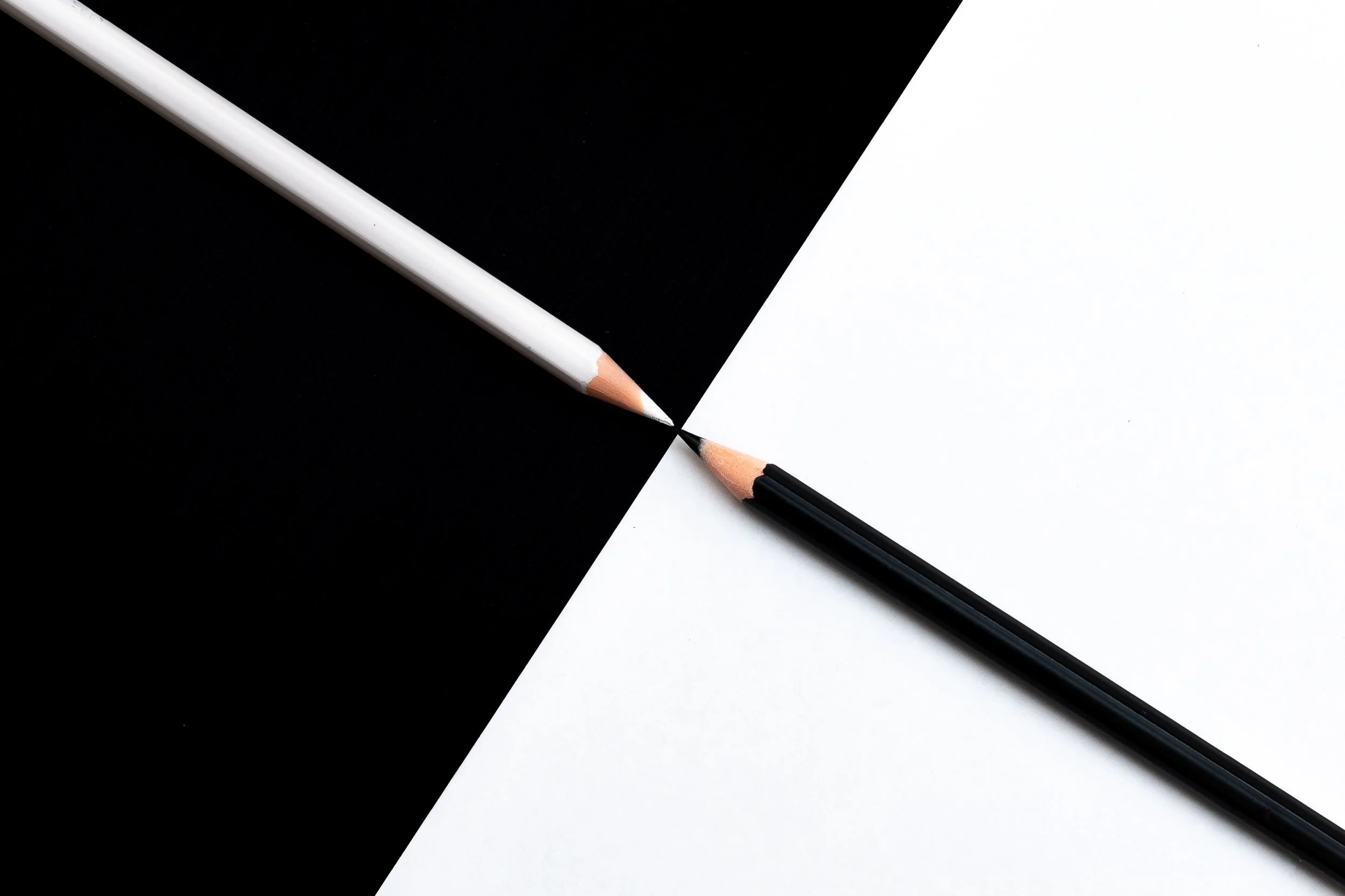 A pencil and a pen placed on a sheet of paper, with the paper divided into black and white sections in a diagonal arrangement.