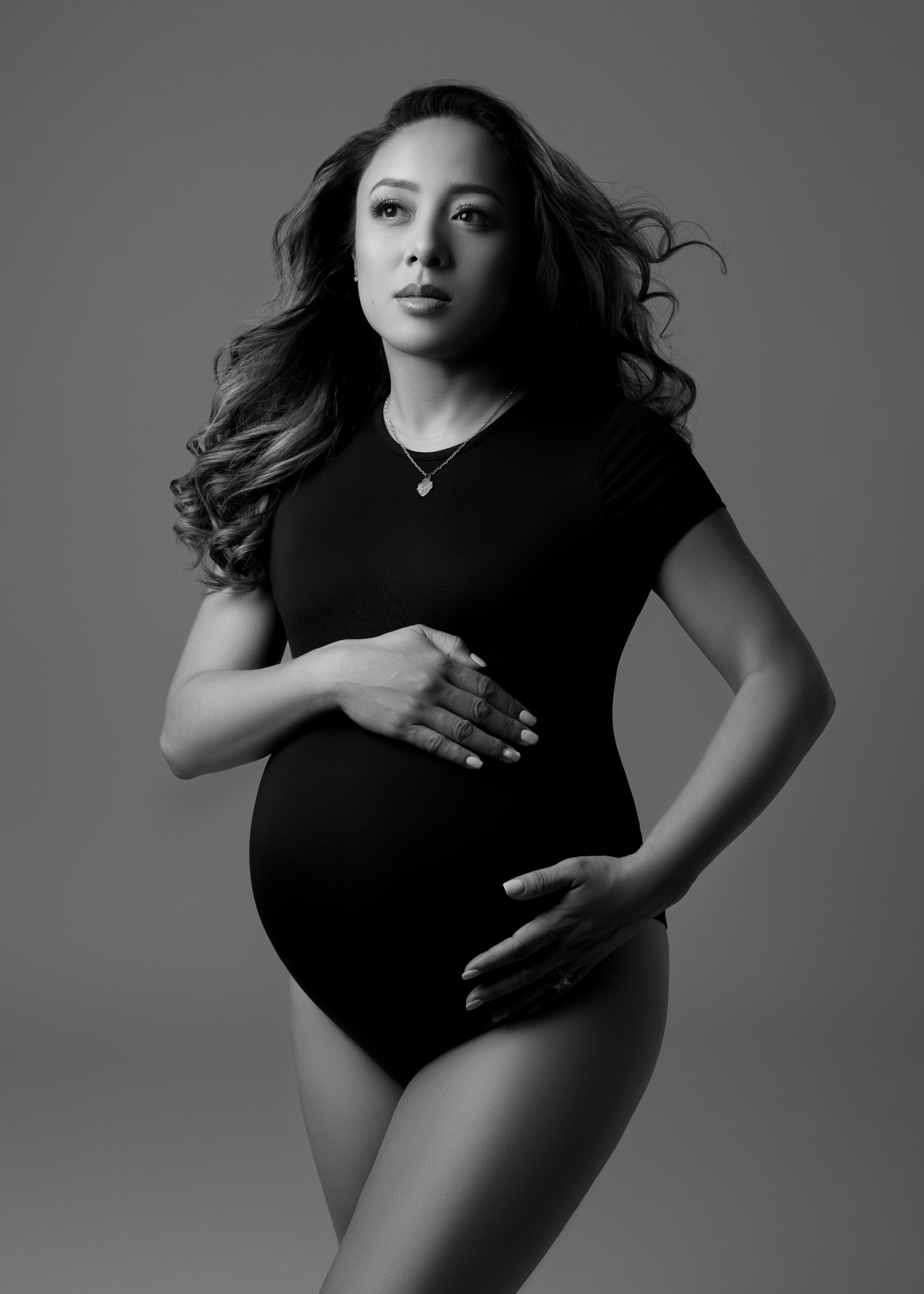 pregnant-woman-in-bodysuit-with-flowing-hair-embracing-baby-bump.jpg