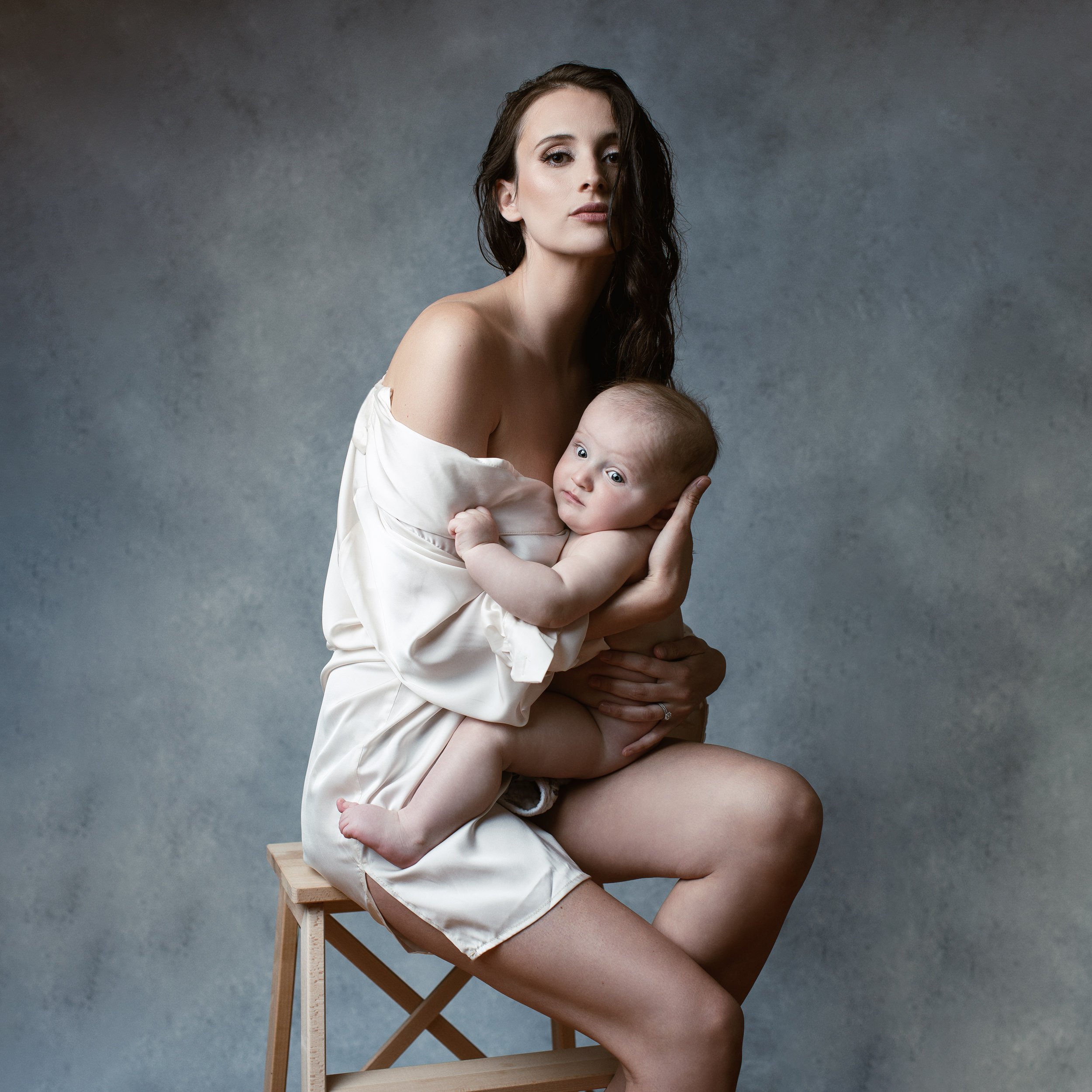 motherhood-photoshoot-with-over-sized-white-collar-shirt-with-wet-hair-holding-her-baby-sitting-on-stool.jpg
