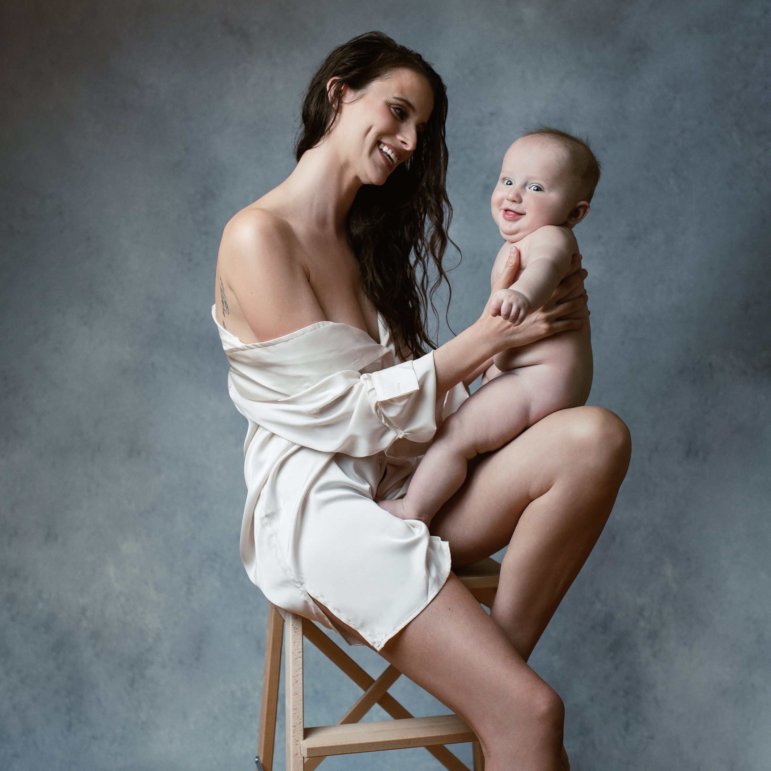 motherhood-photoshoot-with-over-sized-white-collar-shirt-with-wet-hair-holding-her-baby-smiling.jpg