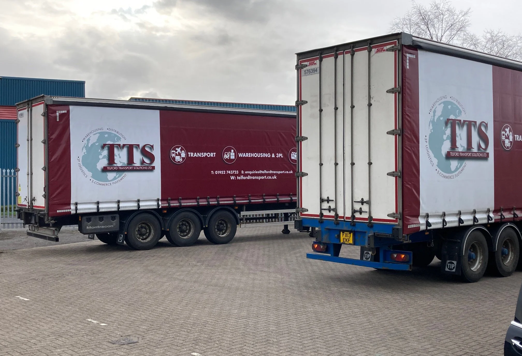 Two large trucks parked in an industrial area, with the side of one truck displaying the Telford Transport Solutions Ltd logo and contact information.