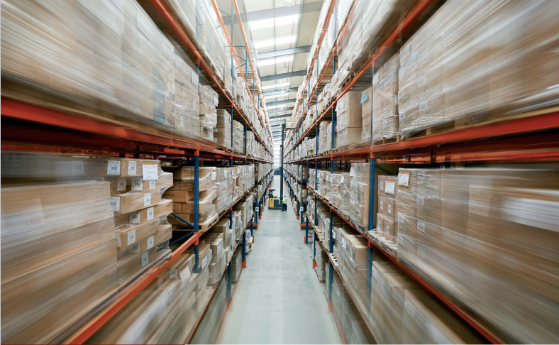 A warehouse aisle with high metal shelves stocked with boxes, and a forklift in the background.