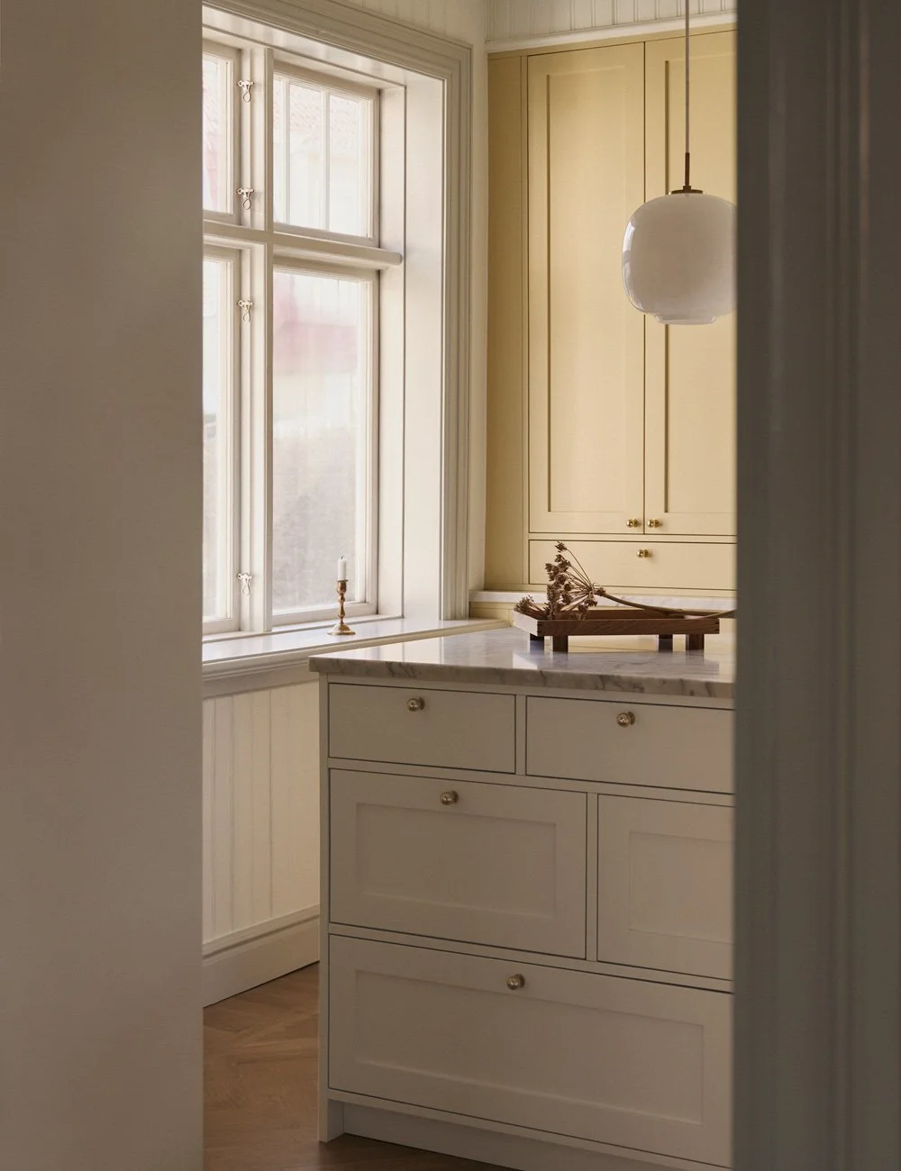 Classic Shaker kitchen with yellow cabinetry, white kitchen island, marble worktop and brass details.