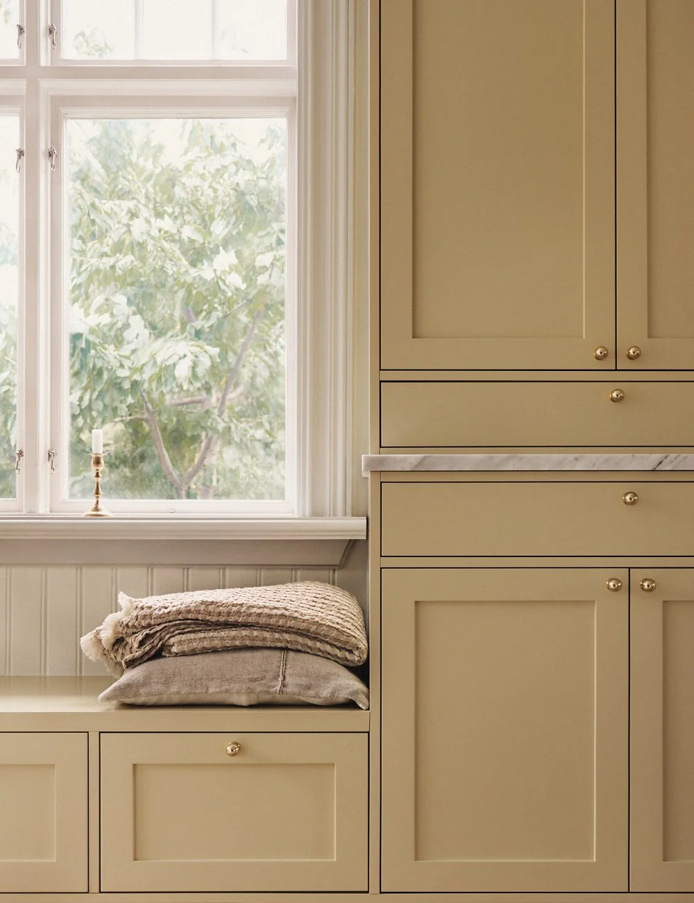 Built-in window seat with integrated storage beneath the window in a yellow Shaker-style kitchen.