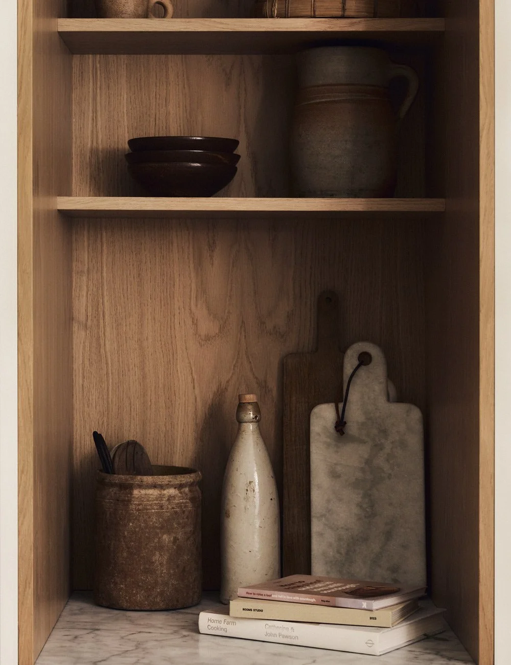 Open oak shelves inside a bespoke kitchen cupboard, with a marble surface at the base.