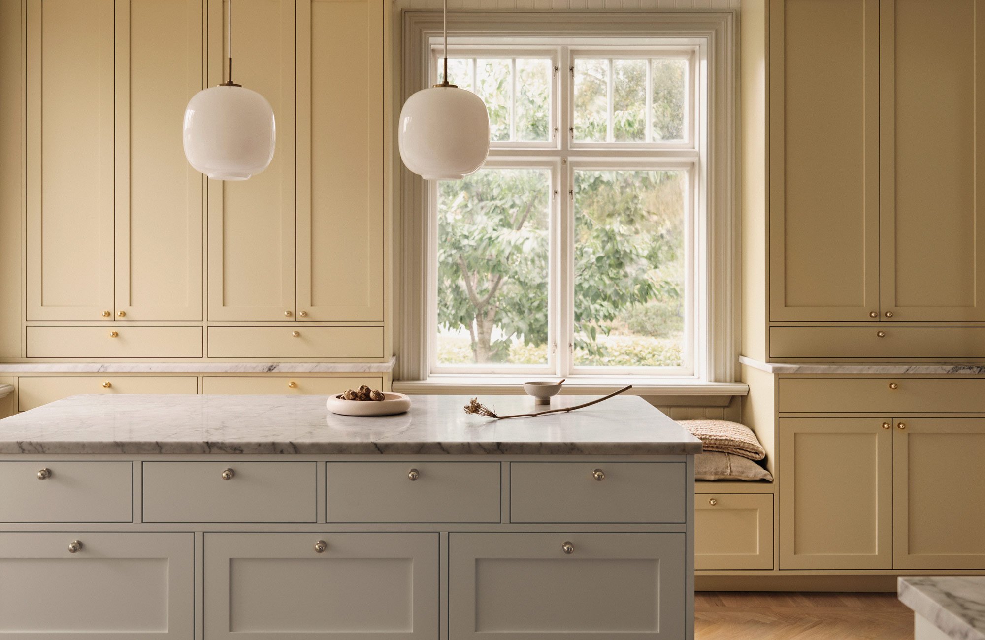 Classic kitchen with bespoke yellow cabinetry, a soft off-white merchant's counter-style island, white Carrara marble worktops and brass knobs.