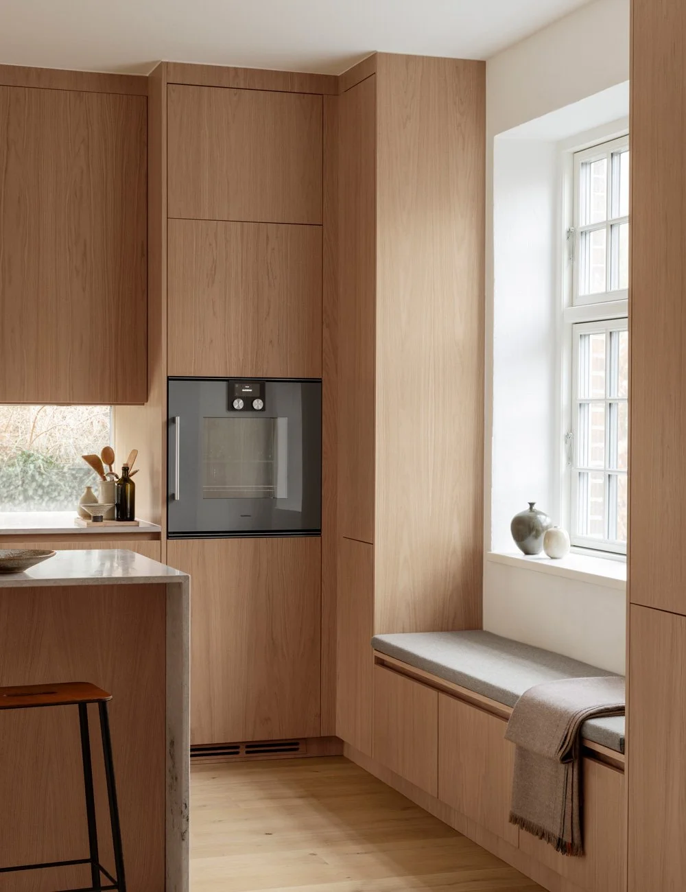 Light oak kitchen with a bespoke built-in window bench and integrated storage.