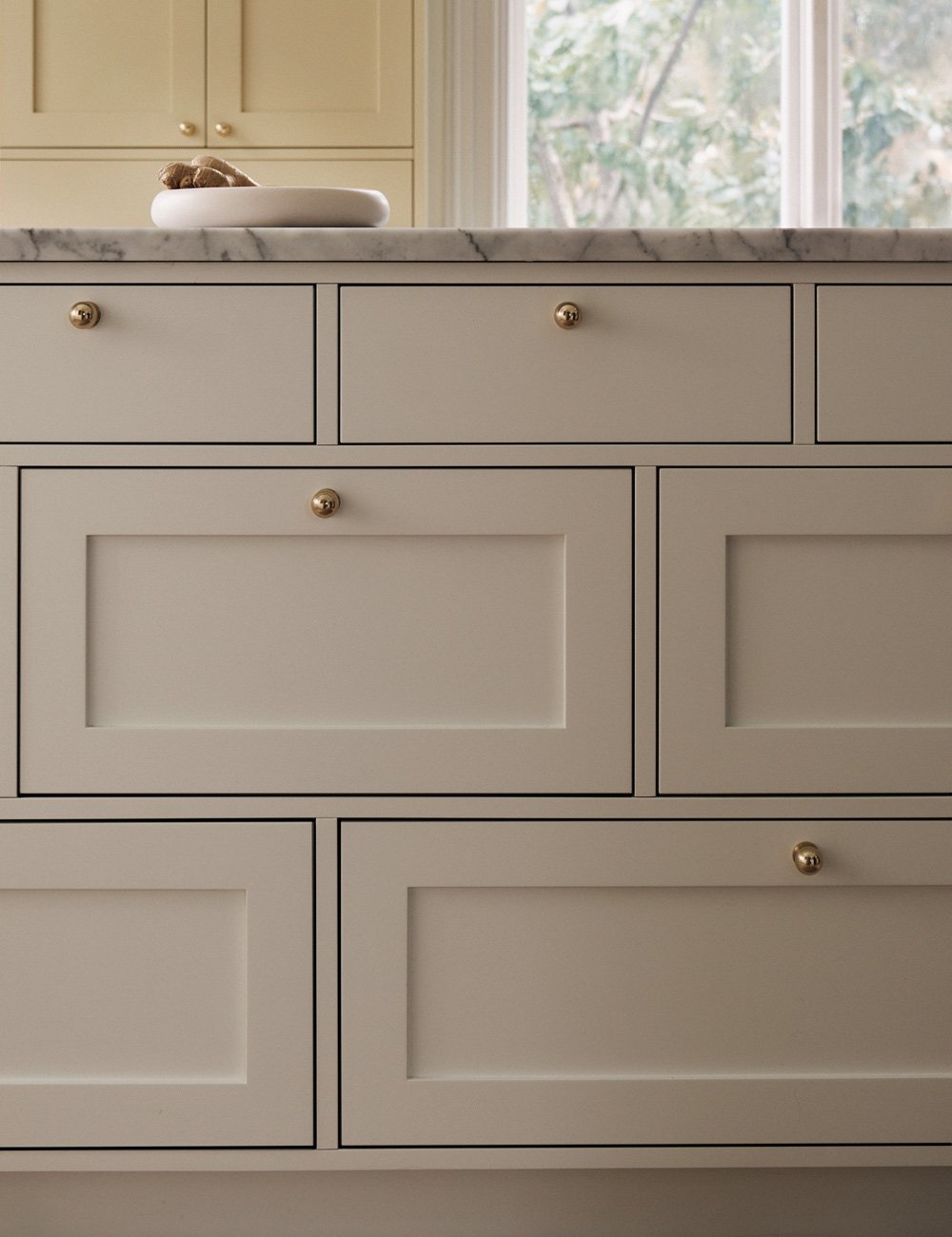 Classic Shaker drawer fronts on a kitchen island, with brass knobs and a white Carrara marble worktop.