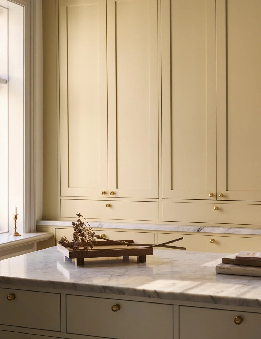 Pale yellow Shaker kitchen cabinets with brass knobs, complemented by soft white cabinetry in a two-tone kitchen design.