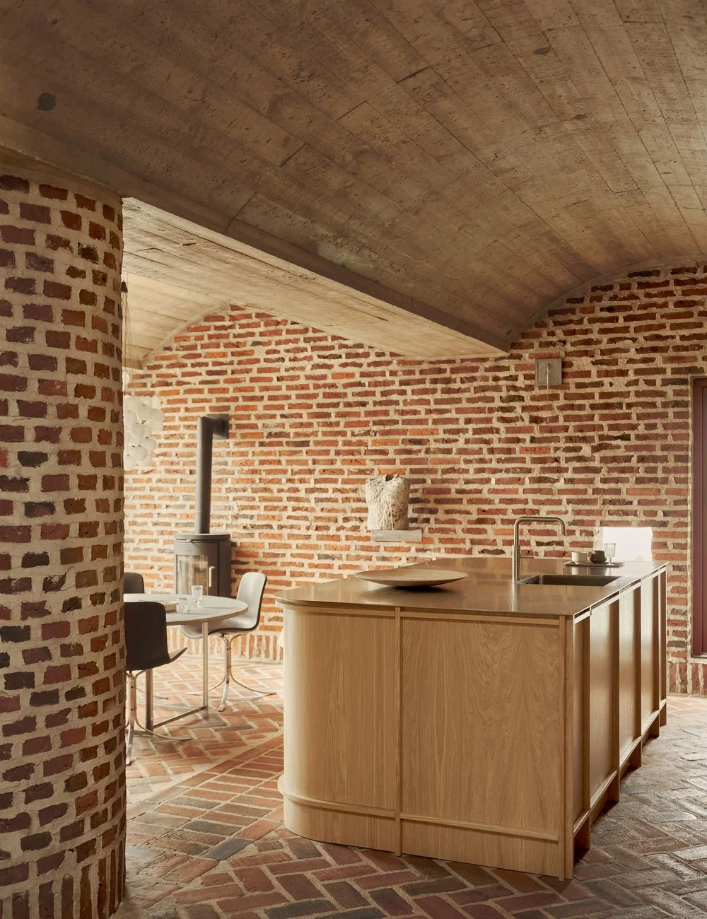 Light oak kitchen island with stainless steel worktop in a modernist brick house with vaulted concrete ceilings.