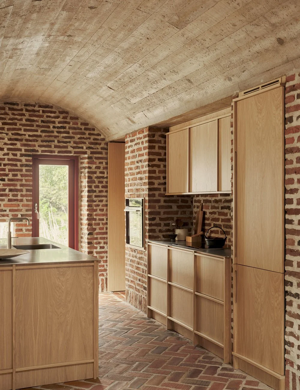 Light oak kitchen cabinetry integrated into an exposed brick wall in a modernist house.