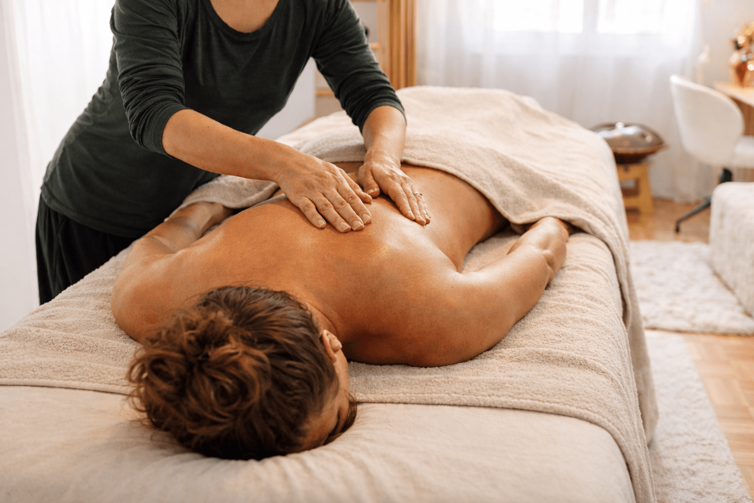 Une personne reçoit un massage sur son dos dans un cadre chaleureux et confortable.