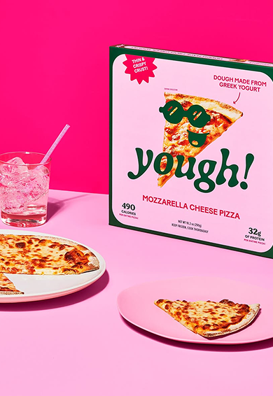 A pink background with a box of 'Yough!' mozzarella cheese pizza, a slice of pizza on a pink plate, and a glass of iced beverage with a straw.