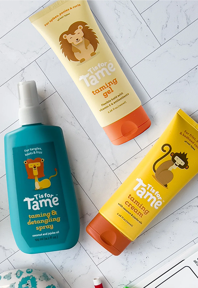 Three bottles of pet grooming products on a white surface. The blue bottle is labeled "Tis for Tame" taming & detangling spray with a lion illustration. The yellow bottle is labeled "Tis for Tame" calming gel with a koala illustration. The third bottle is labeled "Tis for Tame" taming gel with a lion illustration.