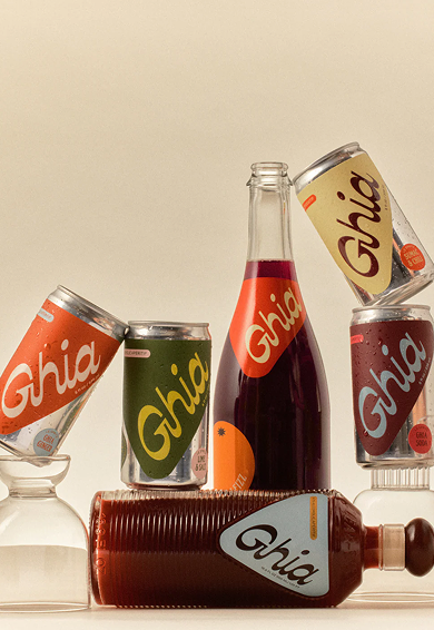 A collection of Ghia non-alcoholic beverage cans, a glass bottle, and a bottle with a dropper cap, all featuring colorful labels and text.