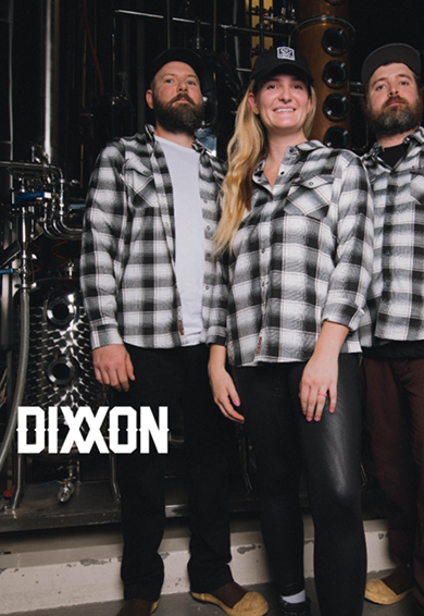 Three people in black and white plaid shirts standing in a music studio with microphones and speakers, with the word 'DIXON' visible in the bottom left corner.