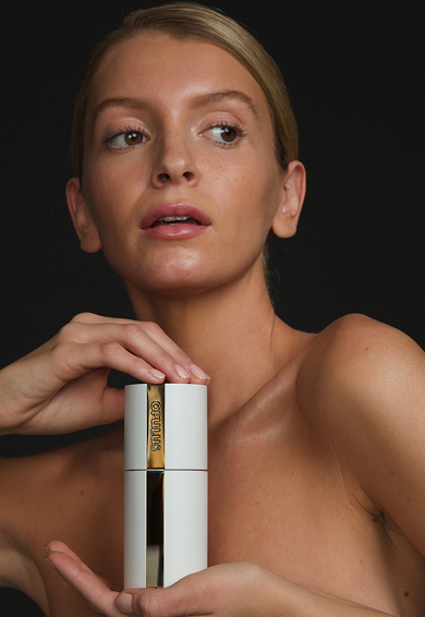 A woman holding a white and gold skincare product tube against a black background.