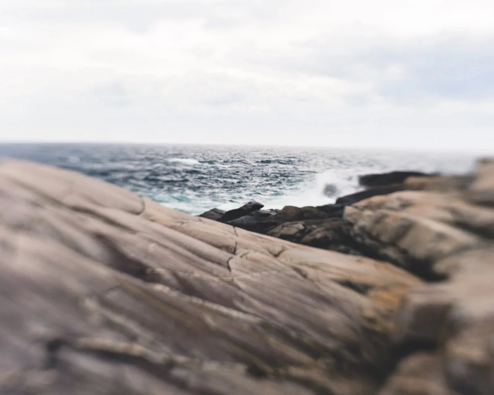 A close-up rocks with a shoreline and ocean in the background, under an overcast sky.