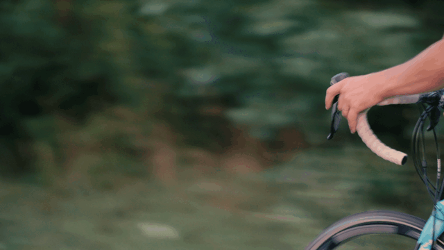A person's hand holding onto the handlebar of a bicycle, with a blurred green background.