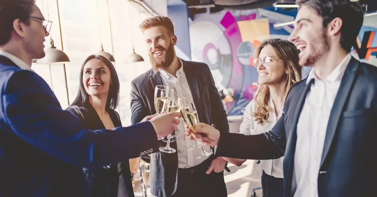 A group of people at a corporate event all wearing business suits. They are clinking their champagne glasses together.