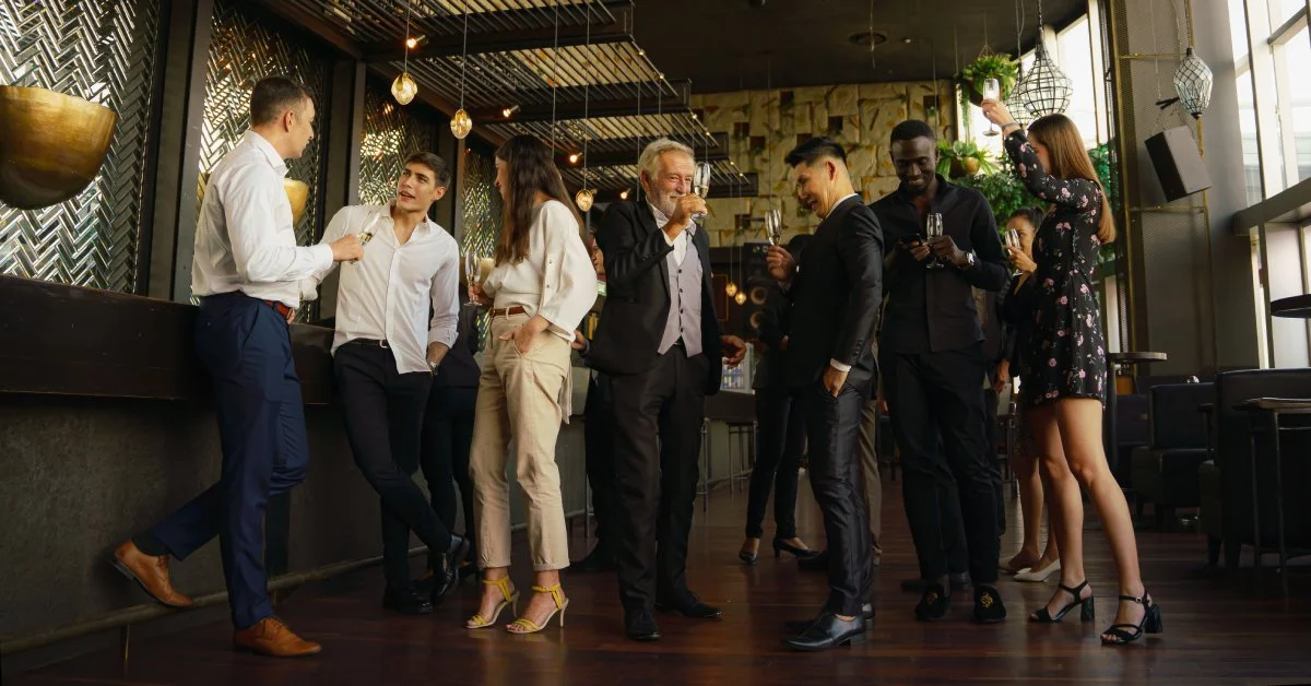 A group of businesspeople standing in a line in a darkly lit restaurant. The people are dressed professionally.